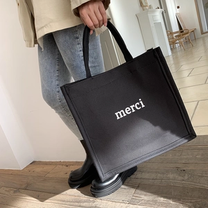Detail of black canvas tote bag featuring white merci print and sturdy fabric handles