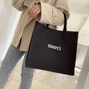 Side view of black canvas tote bag with white merci print on a model in minimalist interior