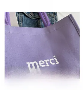 Detailed macro view of purple canvas tote bag with white merci print and woven handle