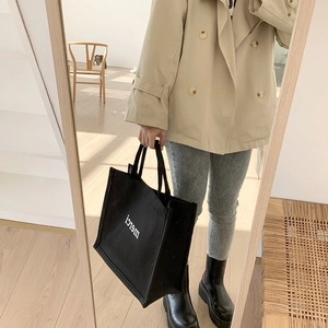 Close-up of black canvas tote bag with white merci print in a mirror selfie styling