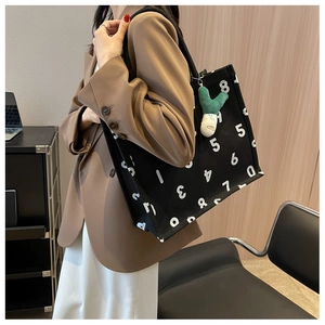 Detail of black canvas tote bag with numeric print and green plush charm accessory