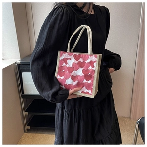Close-up of small linen tote bag with red heart pattern held by woman in black dress