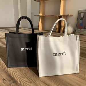 Detail showing black and white canvas tote bags with merci print in a minimalist setting