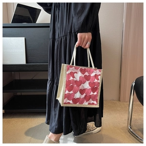 Close-up of linen tote bag featuring woven red and white heart patterns with rope handles