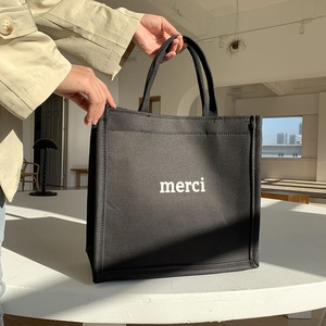 Close-up of black canvas tote bag featuring white merci print and durable fabric texture