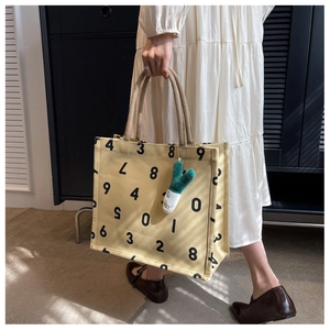 Detail of canvas tote bag with black number prints and plush doll charm accessory