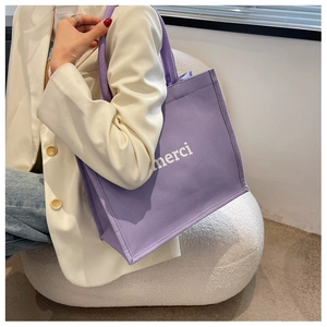 Detail of purple canvas tote bag with white merci lettering and sturdy shoulder straps