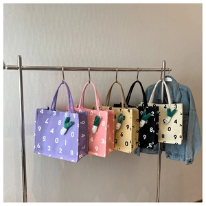 Five assorted canvas tote bags in various colors hanging on a rack with charms
