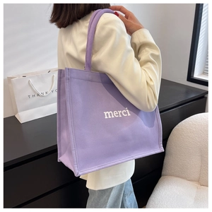 Detail of a purple canvas tote bag with 'merci' print worn by a model in a minimal setting