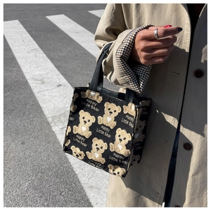 Close-up of black canvas tote with yellow bear prints and leather handle on street