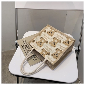 Dettaglio del motivo orso e manico in corda intrecciata su borsa tote in lino beige