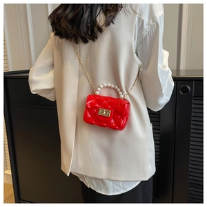 Mini red quilted bag with pearl handle and gold chain strap worn by a child model