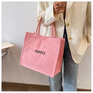 Detailed close-up of a pink canvas tote bag featuring black merci lettering on the front