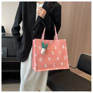Detailed close-up of pink canvas tote bag with white number prints and green plush charm