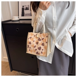 Detail of linen tote bag with heart pattern and white rope handle carried by a model