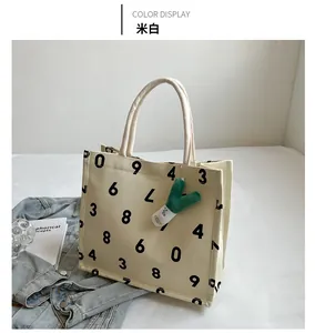 Close-up of off-white large canvas tote bag with numeric print and plush charm accessory
