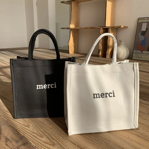 Minimalist canvas tote bags with 'merci' print in black and white colors on wood floor