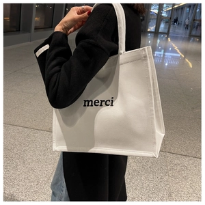 Detail shot of white canvas tote bag featuring black merci print and wide handles