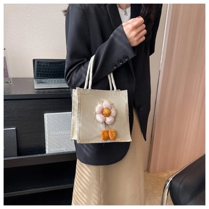 Mini-Tragetasche aus Leinen mit rosa Plüschblume, präsentiert von einem Model im Büro