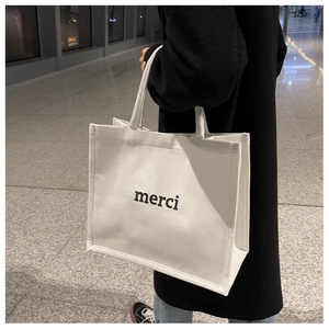 Detail of white canvas tote bag featuring black merci print on a minimalist stylish surface