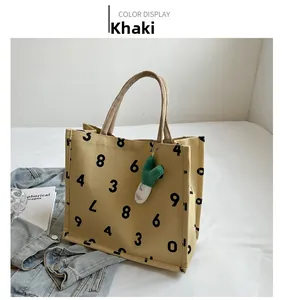 Detail of khaki canvas tote with black numerals, woven handles and green plush charm