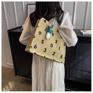 Detail of canvas tote bag with numeric print and plush charm on a woven handle