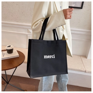 Detail of a large black canvas tote bag with white merci text held by a model