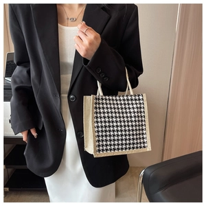 Dettaglio di una borsa tote pied de poule con manici intrecciati beige su una modella