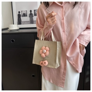 Detail der Leinen-Lunch-Tasche mit süßem rosa Plüschblumen-Anhänger und weißem Griff