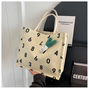Detail of cream canvas tote bag with thick woven rope handles and green scalloped pendant