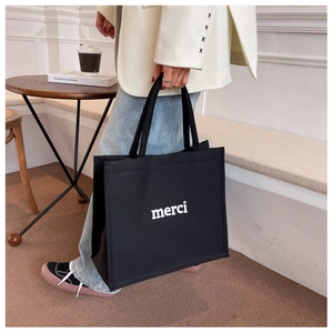Detailed view of black canvas tote bag with white merci print in cafe setting