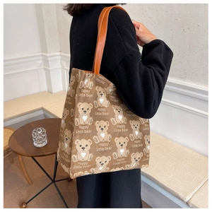 Detail of a brown canvas tote bag with a repeating cute bear pattern and leather handles