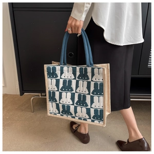 Close-up of beige canvas tote bag with blue rabbit pattern and woven edge detail