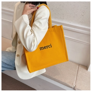 Detail of yellow canvas tote bag with black merci print and woven handles