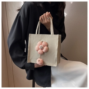 Detailaufnahme der beigen Leinen-Lunchtasche mit dekorativem rosa 3D-Blumenanhänger