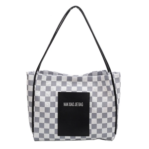 Fashionable checkerboard tote bag with black straps and central logo patch on white backdrop