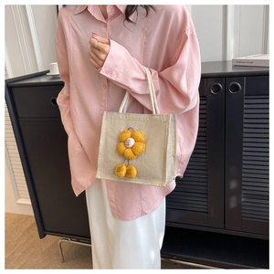 Detail der süßen beigen gewebten Lunchtasche mit gelber Blume und flauschigen Pompon-Anhängern