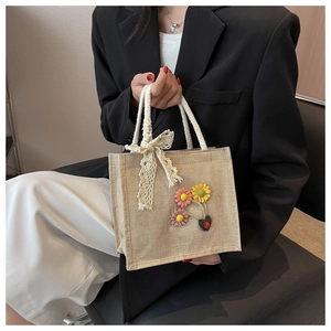 Close-up of linen handbag featuring lace bow, floral accents and sturdy rope handles