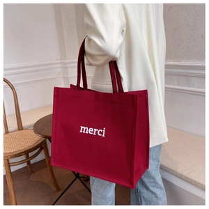 Deep red canvas tote bag with white merci print shown in a stylish lifestyle setting