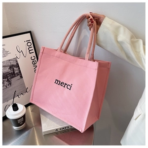 Detail view of pink canvas tote bag featuring merci print with durable woven handles