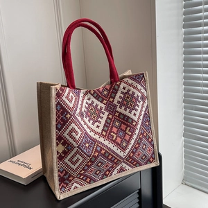 Ethnic embroidery tote bag with geometric patterns and red woven handles on dark shelf