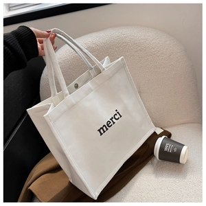 Detail of white canvas tote bag featuring merci print and metal snap button closure