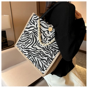 Detail of zebra pattern tote bag featuring decorative pearl chain and woven edge trim