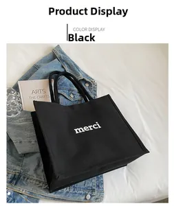 Close-up of black canvas tote bag with white merci text in a lifestyle setting