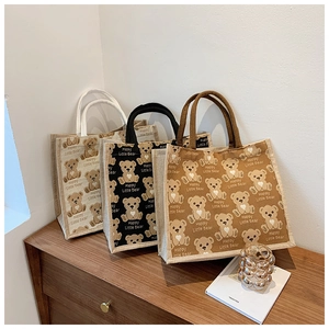 Detailed close-up of three jute tote bags with bear print on a wooden shelf