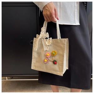 Linen tote bag detail with cotton rope handles, lace bow, and decorative fabric flowers