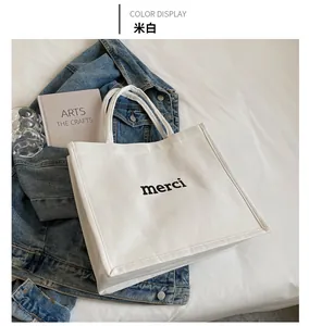 Detail of off-white canvas tote bag featuring black merci print on a white bed