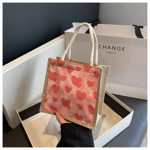 Close-up of a jute bento lunch bag with pink dye and red hearts featuring cotton rope handles