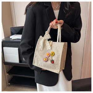 Close-up of beige linen handbag featuring 3D floral accents and a white lace bow detail