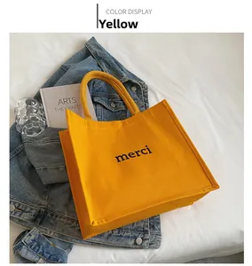 Detailed view of yellow canvas tote bag with black merci print on a soft white bed
